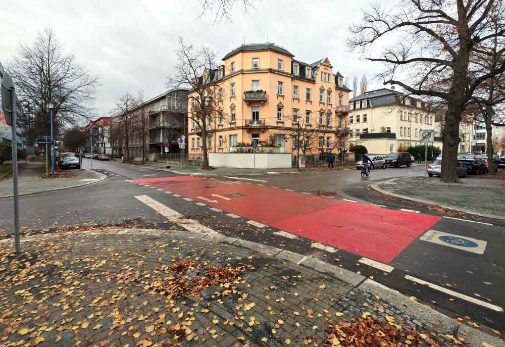 Arbeiter haben ab September 2025 die Kreuzung der Radroute Ost mit der Bärensteiner Straße verkleinert. Die vergrößerten Gehwege sind vorn, hinten links und rechts zu sehen. Am orangen Eckhaus wurden statt dessen Parkverbote eingerichtet. Foto: Heiko Weckbrodt