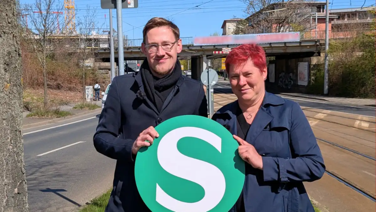 Stefan Engel und Dana Frohwieser werben mit einem S-Bahn-Schild für ihren Plan, an der Kreuzung von Teplitzer Straße und Bahnstrecke einen neuen Halt einzurichten. Foto: SPD-Fraktion Dresden